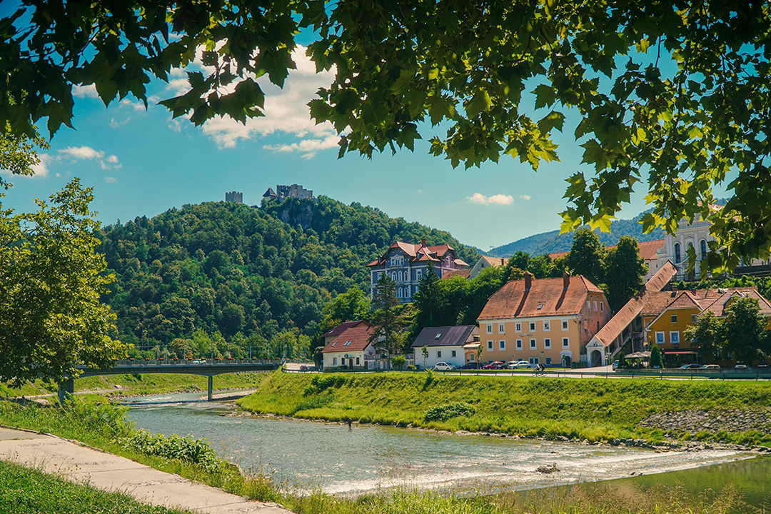 A view of Celje beside the Savinja River and Celje Castle rising above the town on a wooded hill.