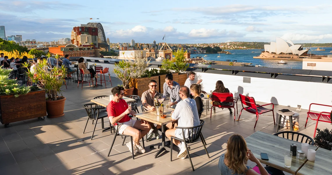 Guests socialising on a hostel terrace overlooking Sydney Harbour.