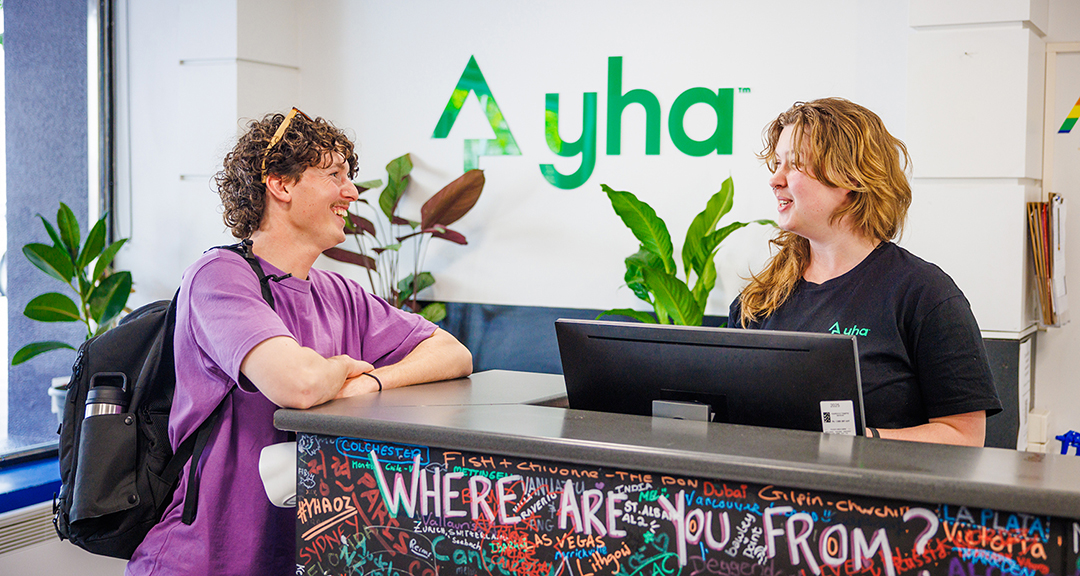 Guests chatting with staff at the reception of a YHA hostel.