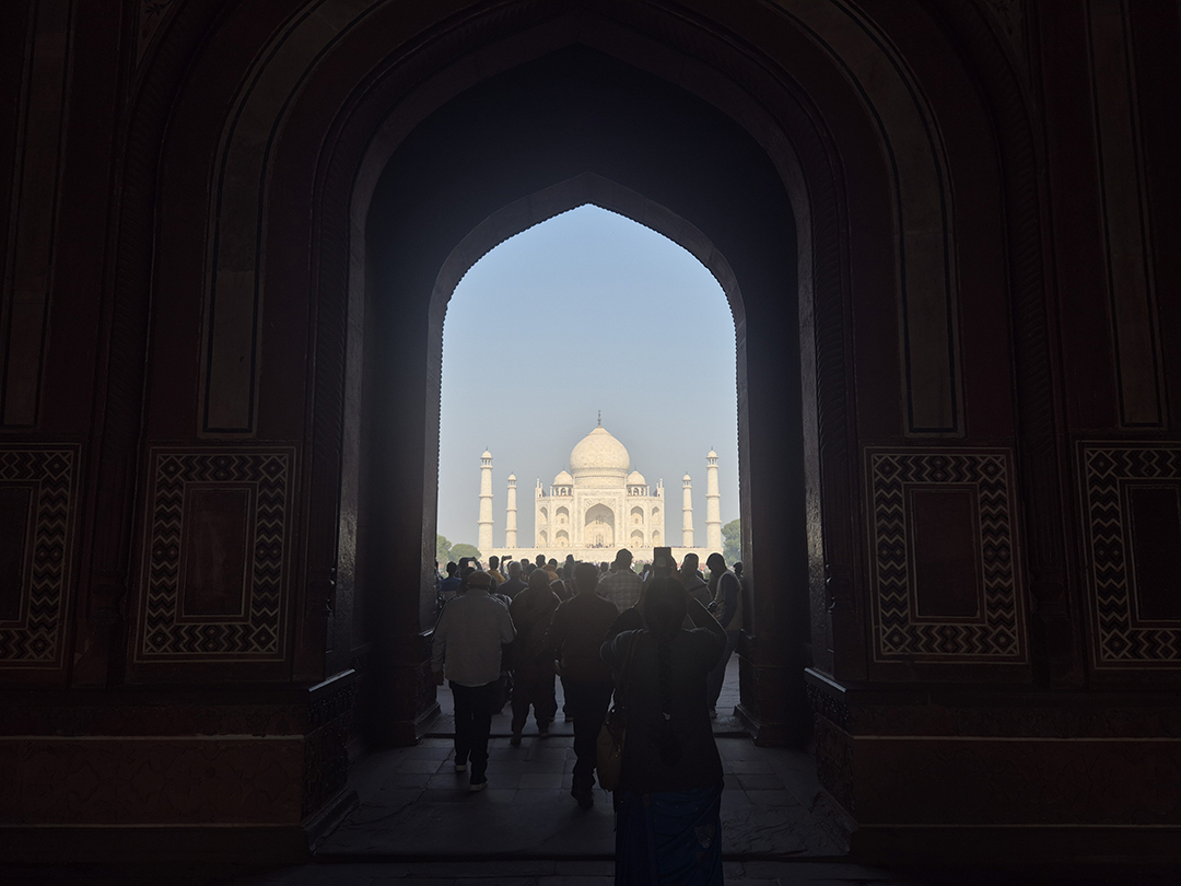 View of the Taj Mahal through the monumental entrance gateway in Agra with visitors walking toward one of the most famous landmarks in India.