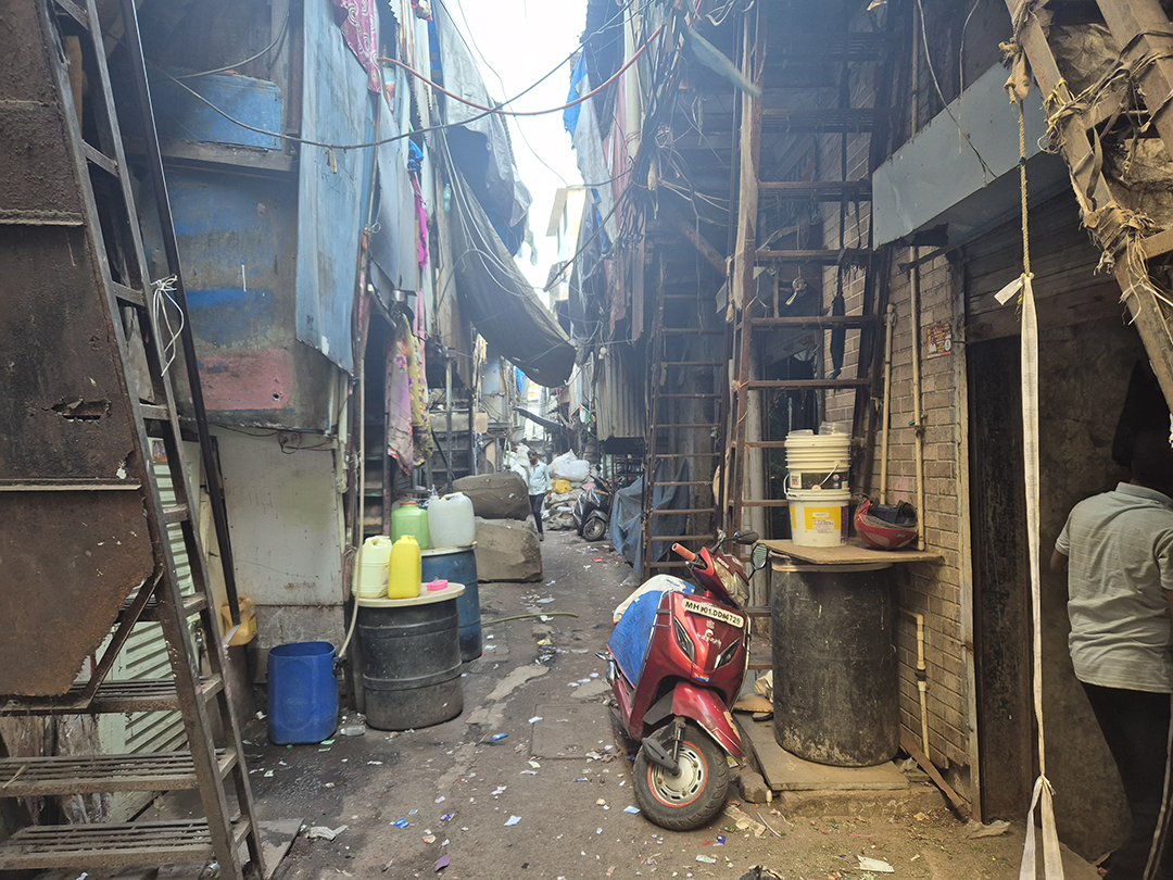 Narrow street in a Mumbai slum with improvised buildings, motorbike and everyday life in one of the largest cities in India.