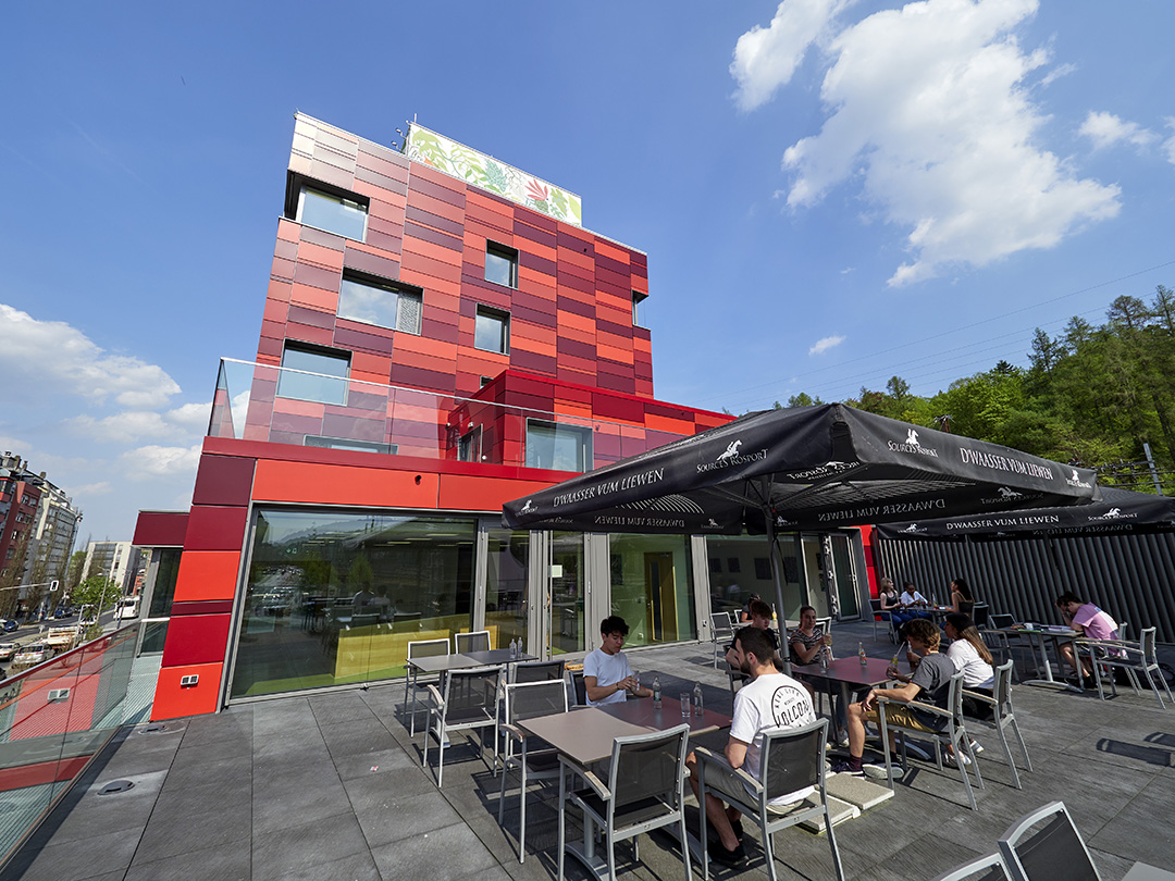 Modern red building of a youth hostel in Esch-sur-Alzette with an outdoor terrace in an urban setting.