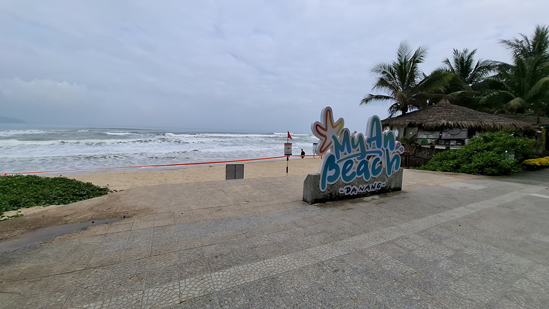 My Khe beach in Da Nang Vietnam with waves of the South China Sea, palm trees and the My An Beach sign along the coast.
