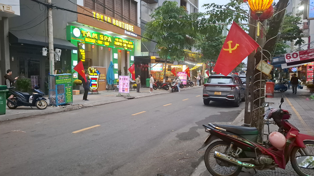 Street scene in Da Nang Vietnam with local shops, motorbikes and Vietnamese flags displayed along the road.