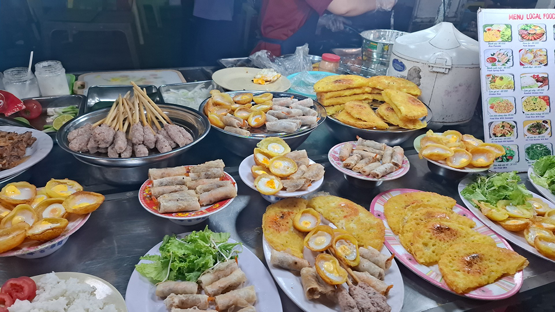 Traditional Vietnamese street food dishes at a market stall including spring rolls, egg dishes and rice specialties.