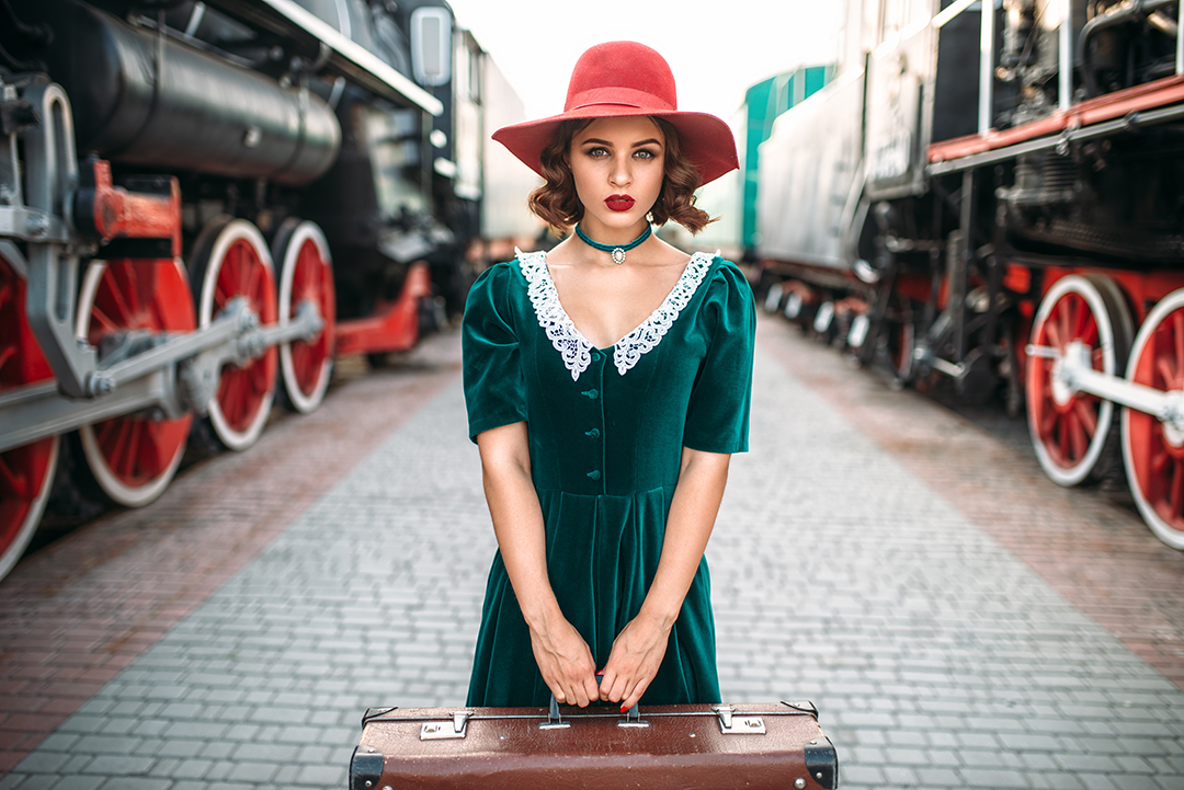Ženska v elegantni vintage obleki s starim kovčkom ponazarja trajnostno modo, ponovno uporabo oblačil in brezčasen potovalni slog.